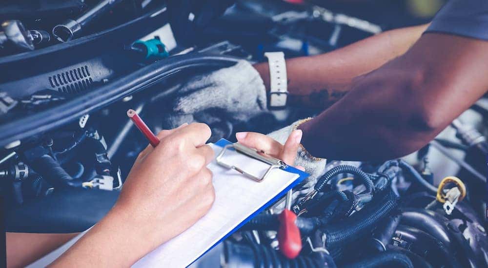 A close up shows a person with a clip board and a mechanic servicing a used Jeep.