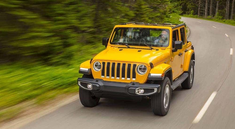 A yellow 2021 Jeep Wrangler is driving down the street past blurred trees after leaving a Jeep dealer near you.