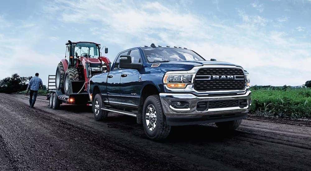 A blue 2024 Ram 2500 HD is shown from the front at an angle while towing a tractor.