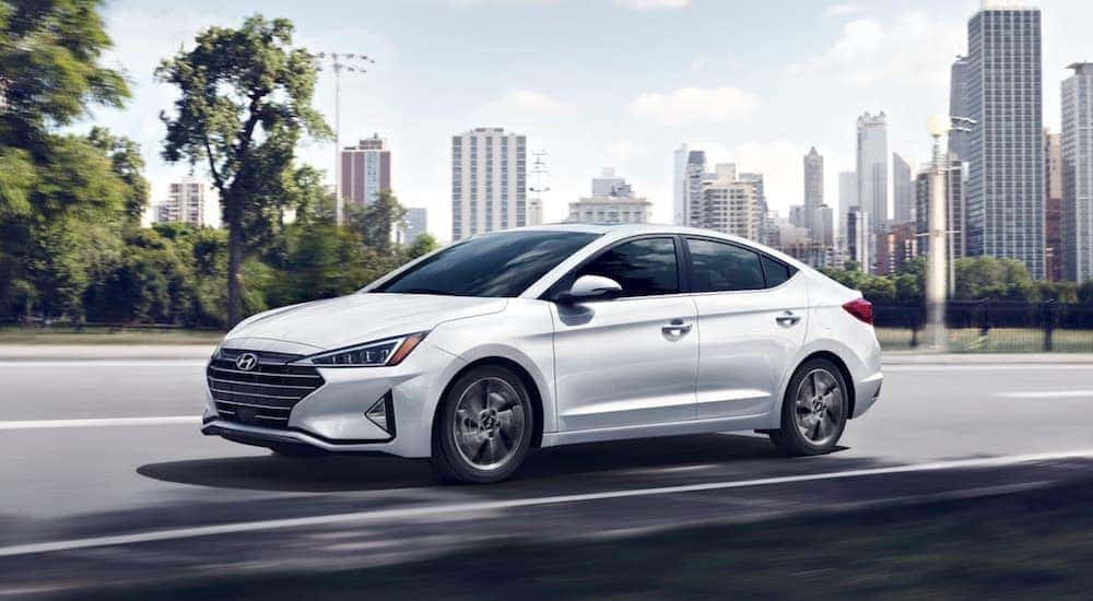 A white 2020 Hyundai Elantra is shown driving on an open road past a city.