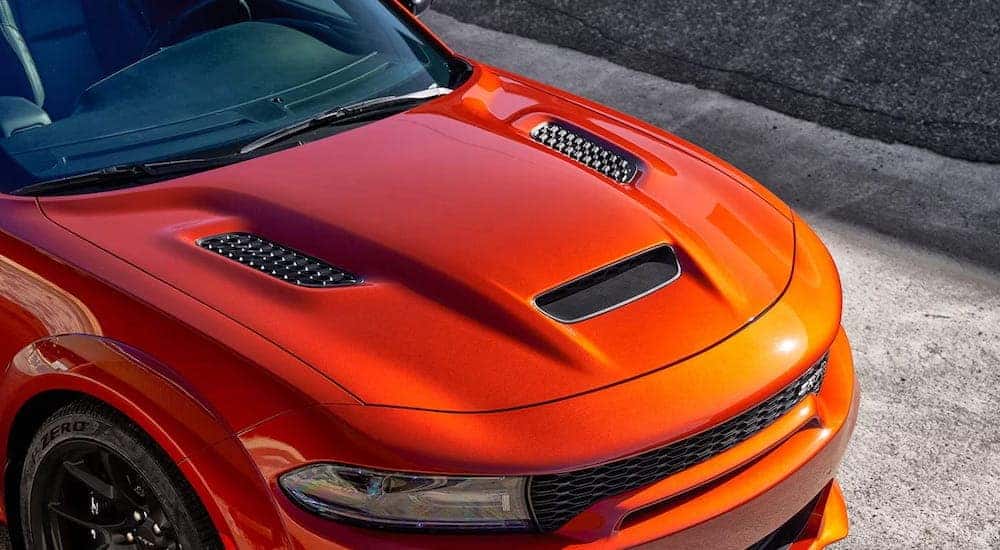 A close-up shows the hood of an orange 2023 Dodge Charger Hellcat Wide Dody.
