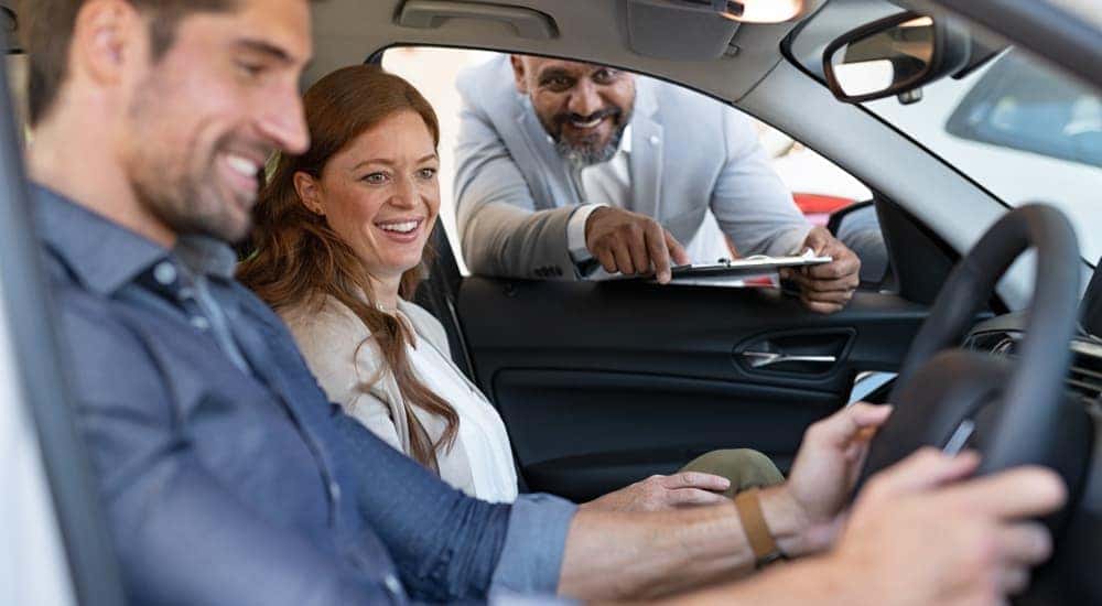 A couple is in a car while a salesman shows them features.