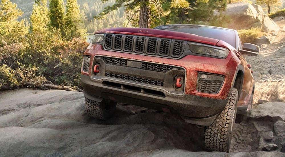 A red 2023 Jeep Grand Cherokee Trailhawk is shown from the front while it climbs a hill.