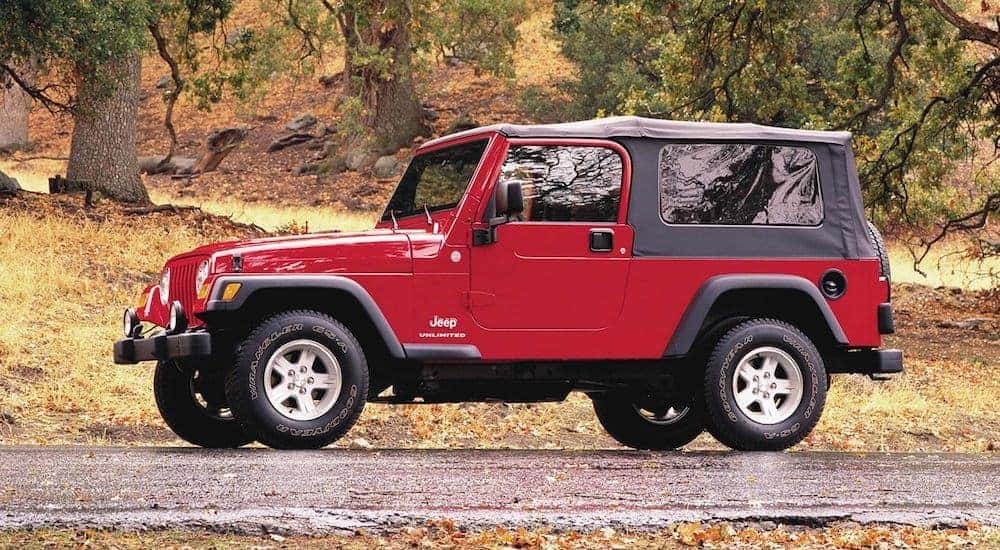A red 2005 used Jeep Wrangler is parked with trees in the background.