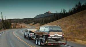 A silver 2020 Jeep Gladiator is shown towing a Wagoneer down the road.