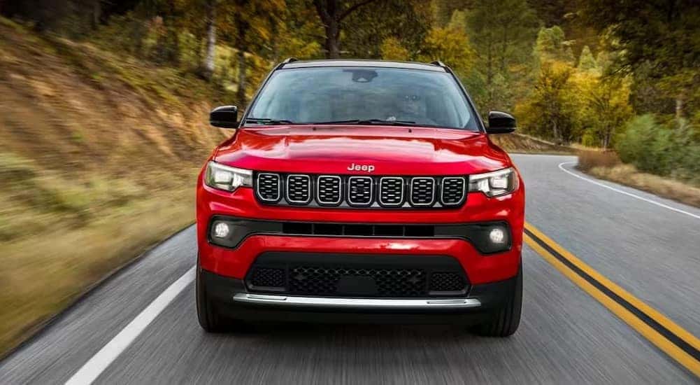 A red 2024 Jeep Compass for sale is shown driving on a highway.