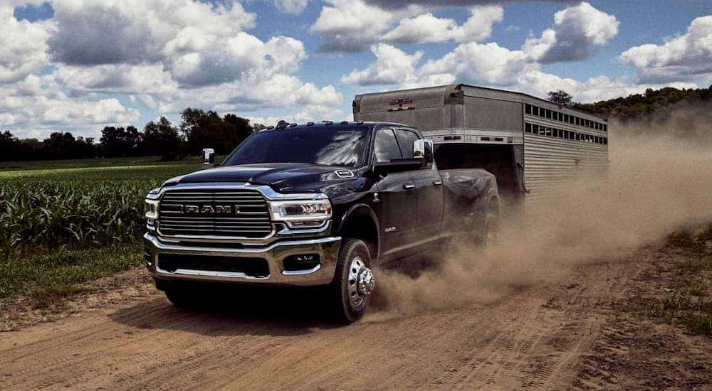 A black 2020 Ram 3500 is towing a horse trailer on a dirt road past fields near Lexington, KY.