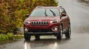 A burgundy 2020 Jeep Cherokee is shown using its automatic windshield wipers on a rainy street.