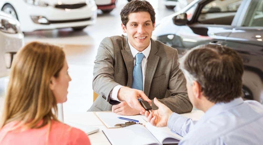 A close up shows a sales man handing a set of car keys to a couple.