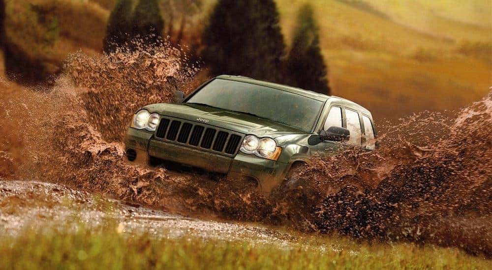 A green 2011 used Jeep Grand Cherokee is driving through a mud puddle.