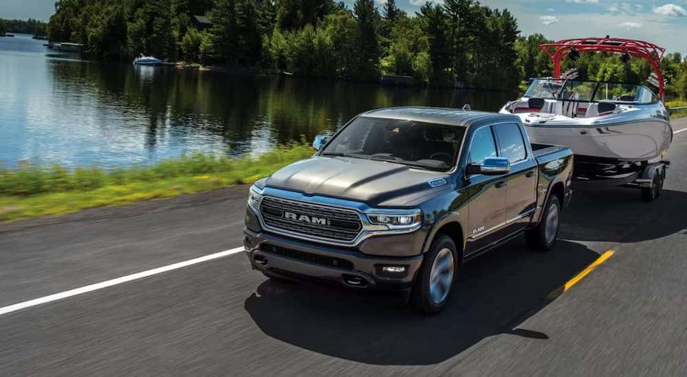A grey 2023 used Ram 1500 for sale is shown towing a boat next to a lake.