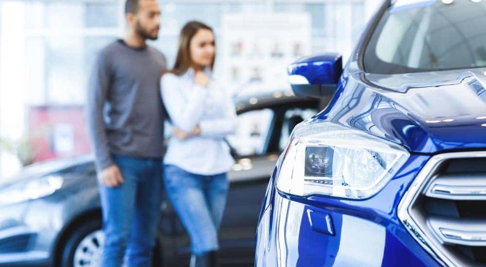 An out of focus couple is looking at used vehicles for sale in a showroom.