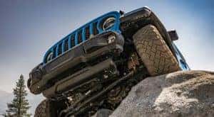 A blue 2022 Jeep Wrangler Rubicon Extreme Recon is shown from a low angle climbing a rock.