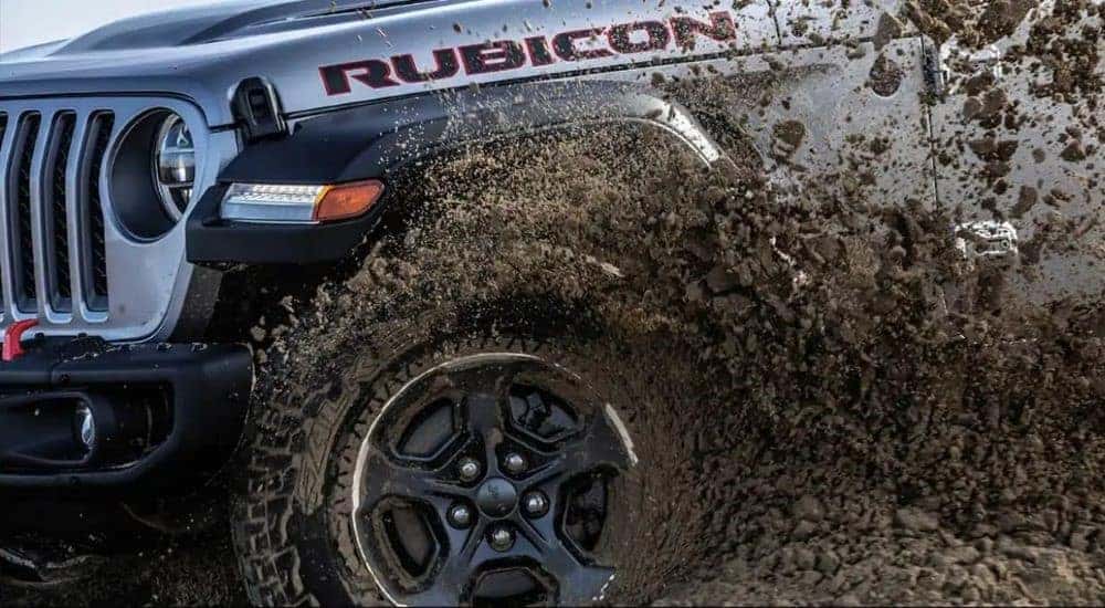 A silver 2023 Jeep Gladiator Rubicon is shown driving on muddy terrain.