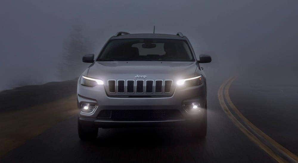 A grey 2019 Jeep Cherokee is driving on a dark foggy road near Lexington, KY.