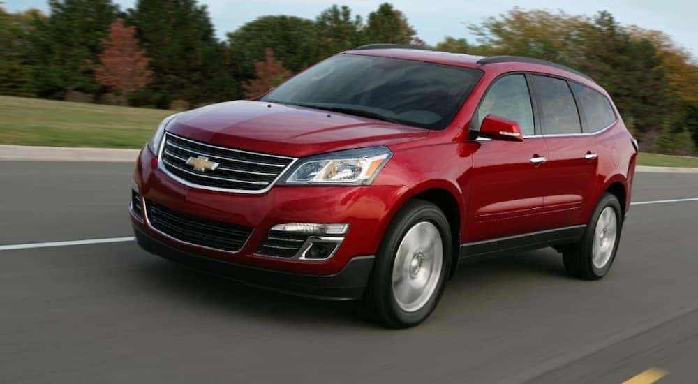 A red 2013 Chevy Traverse, which is popular among used cars near me, is driving on a highway past trees.