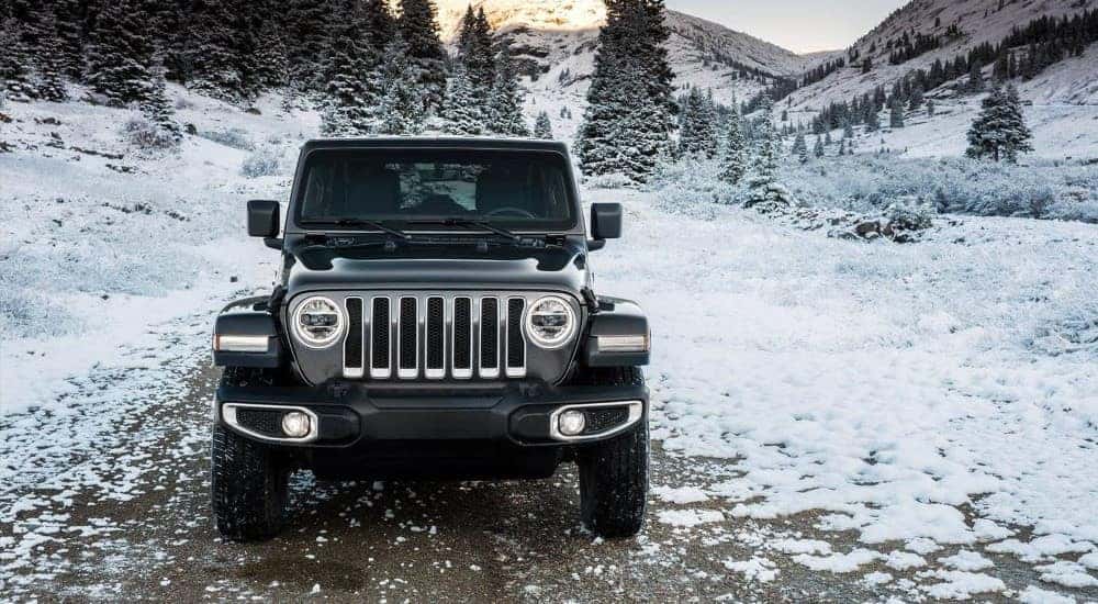 A front view of a black 2024 Jeep Wrangler parked off-road on a snowy trail.