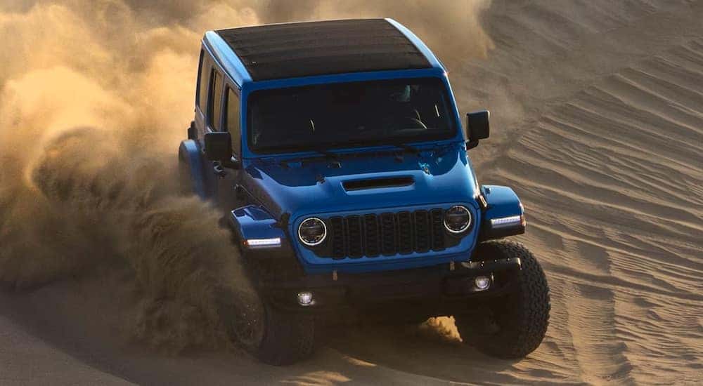 A blue 2024 Jeep Wrangler driving through a desert.