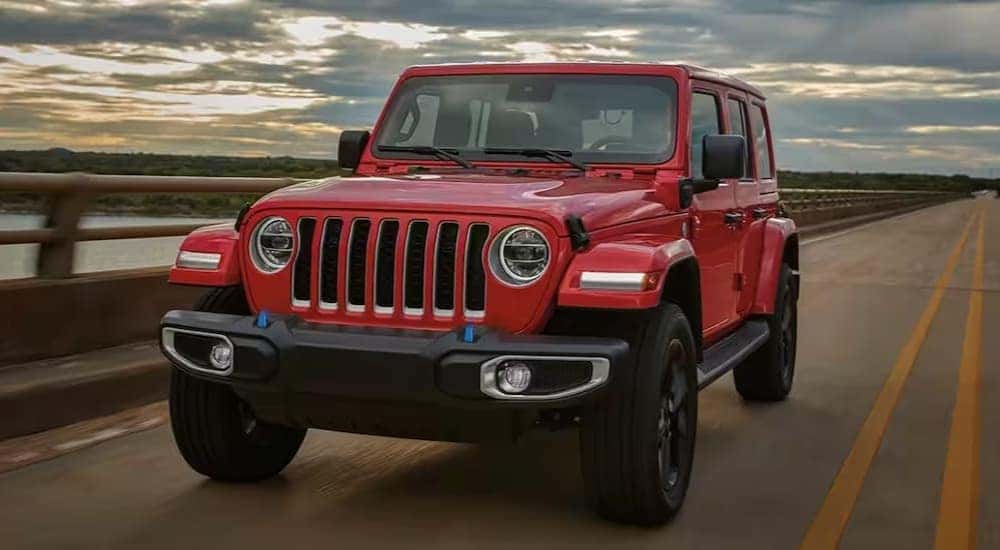 A red 2023 Jeep Wrangler is shown driving on a bridge after viewing a used Jeep Wrangler for sale.