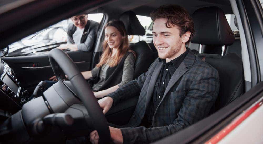 A couple is sitting in a used car at a Lexington dealership while a sales person talks to them.