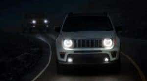 A white 2020 Jeep Renegade is shown at night with its smart headlights illuminated after leaving a used car dealership in Lexington.