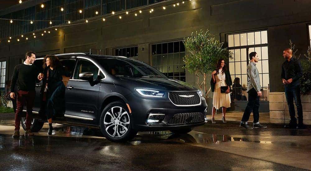 A dark grey 2021 Chrysler Pacifica is shown from the side parked outside of a restaurant.