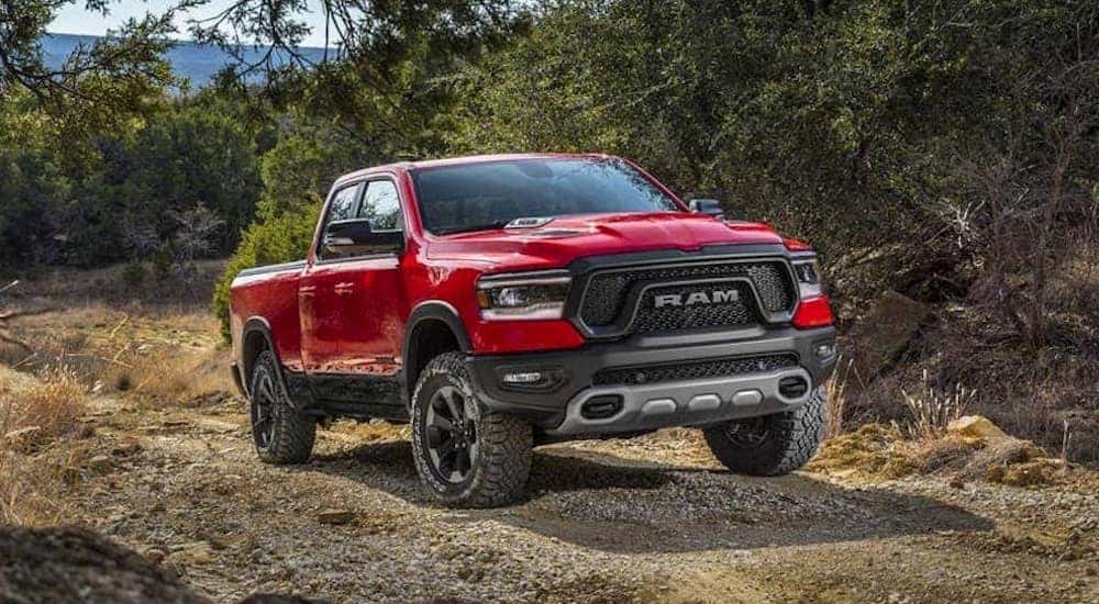 A red 2019 used Ram 1500 is driving on a dirt trail past trees.