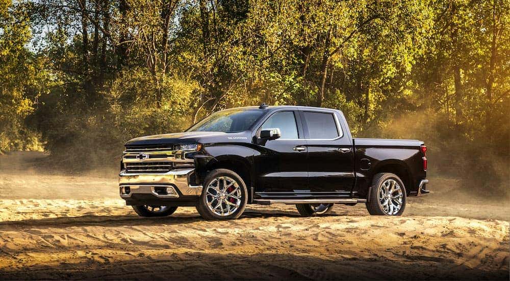 A black 2019 Chevy Silverado 1500 is shown from the side parked on the dirt with dust in the air.
