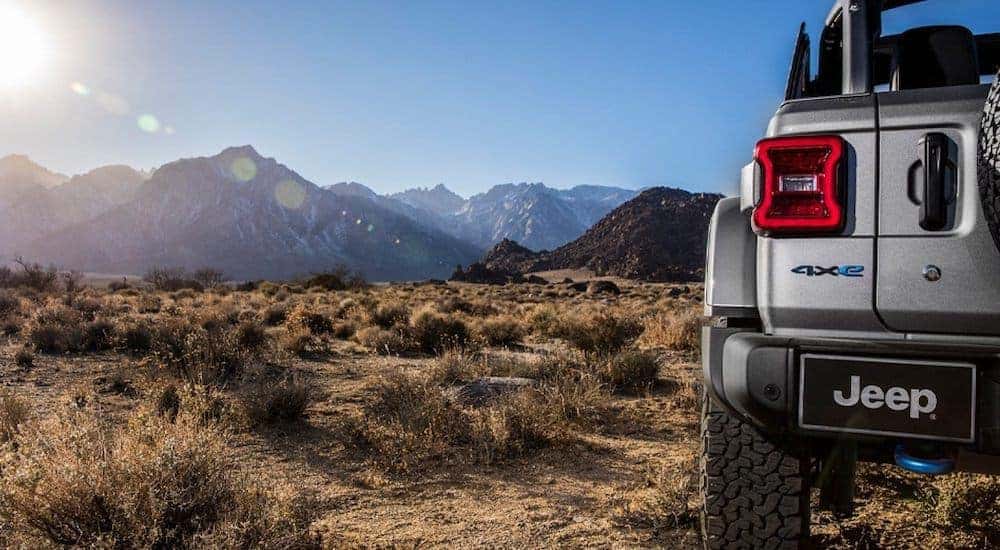 A grey 2021 Jeep Wrangler 4xe is shown from the rear in the desert with mountains in the distance.