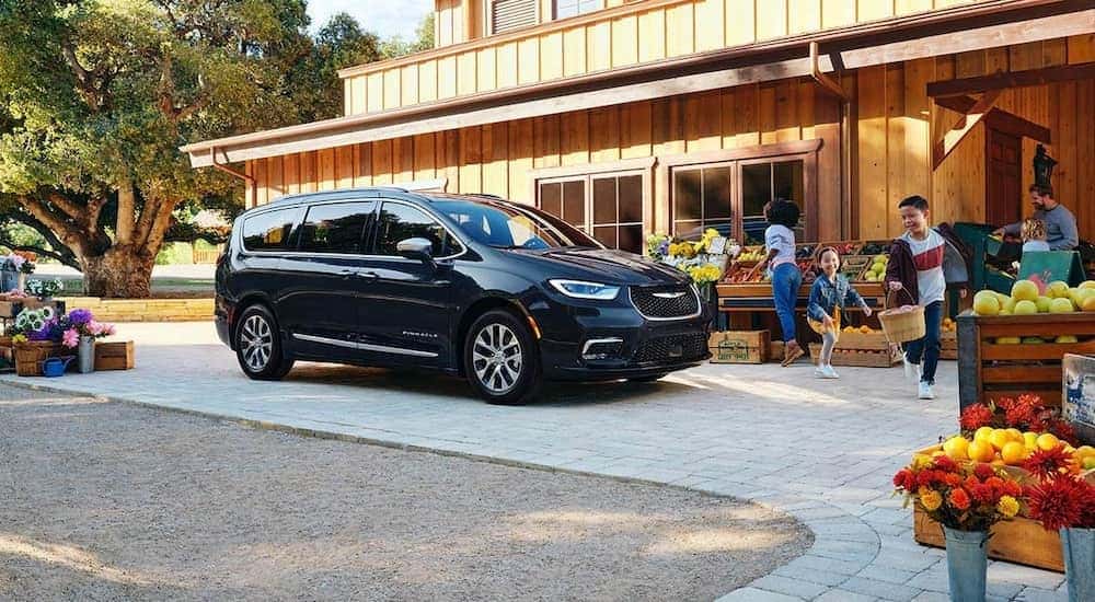 A black 2021 Chrysler Pacifica Hybrid is shown from the side, parked at a farmers market.