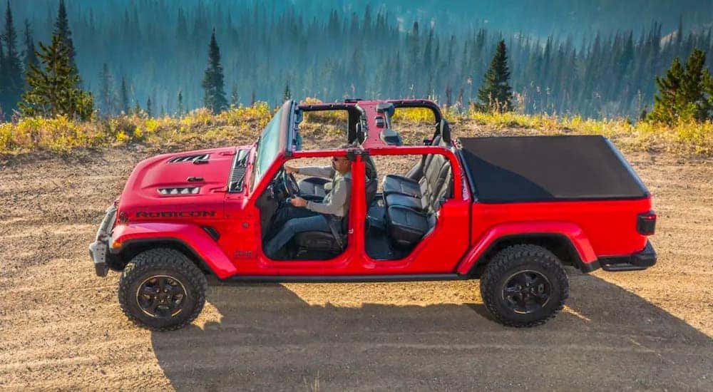 A red 2019 Jeep Gladiator with no roof or doors is shown from a high angle while driving on a mountain road.