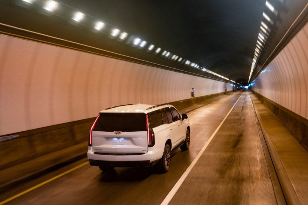 Rear 3/4 view of 2023 Cadillac Escalade Sport in Crystal White Tintcoat driving through a tunnel