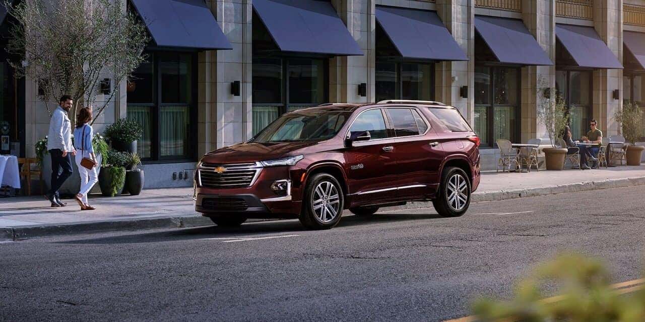 Maroon 2023 Chevy Traverse High Country Parked on side of the road. Passengers walking by