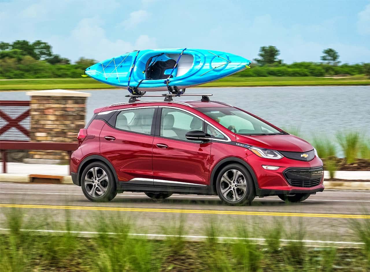 Red 2017 Chevrolet Bolt Ev driving down road with blue kayak on top