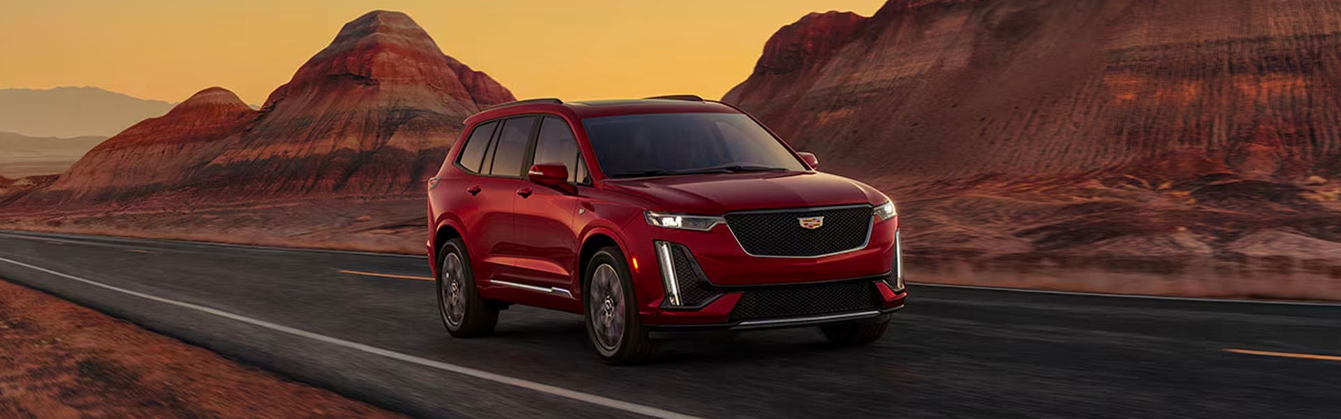 A red 2025 Cadillac XT6 luxury SUV driving on an open desert highway at sunset