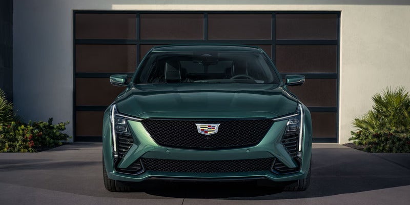 Front view of a sleek, green Cadillac CT5-V parked in a driveway. The car's bold design features angular headlights and a prominent grille, exuding a modern luxury vibe.
