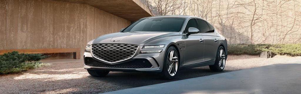 Silver 2026 Genesis G80 luxury sedan parked in front of a modern architectural building, showcasing its elegant design and performance-focused styling.