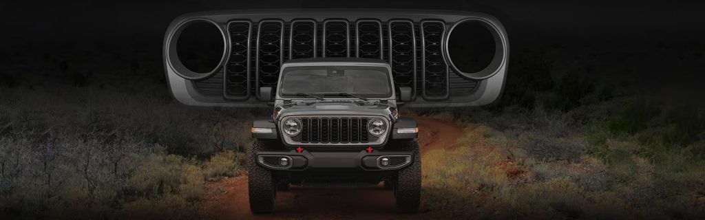 Front view of a rugged off-road SUV on a dirt trail with a dramatic oversized grille backdrop.