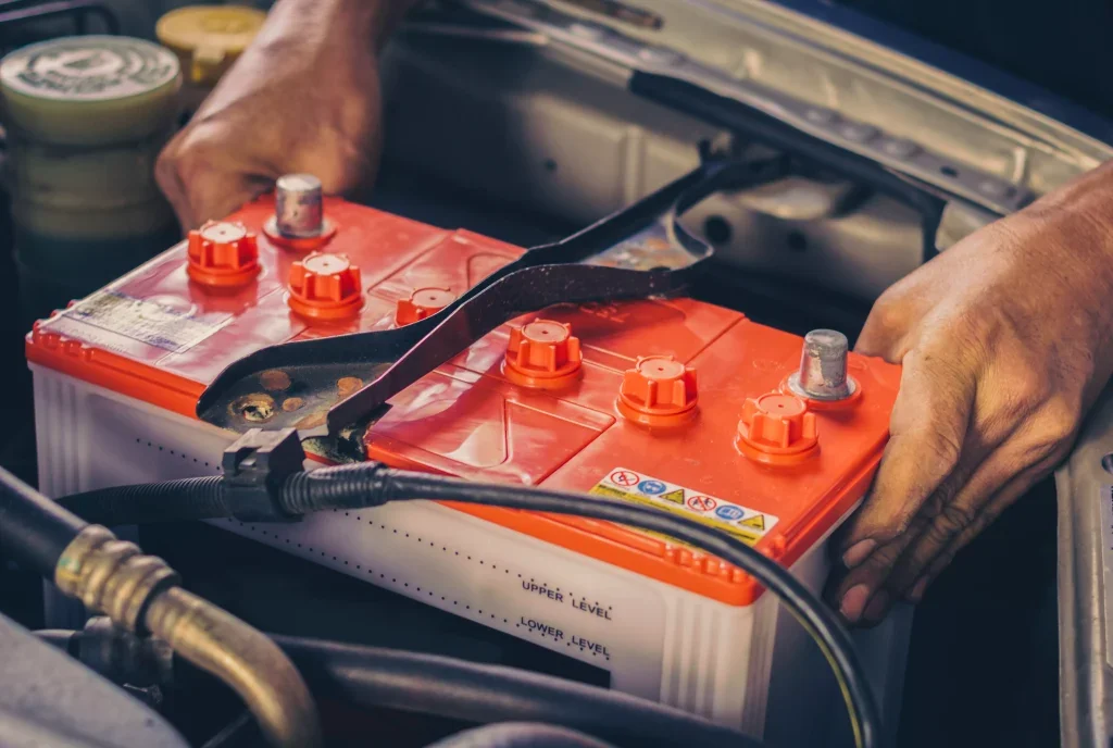 Mechanic working on a car battery under the hood.