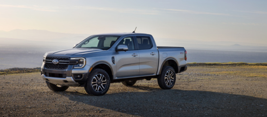 A silver pickup truck is parked on a rocky terrain with a clear sky and distant mountains in the background, conveying a sense of rugged adventure.