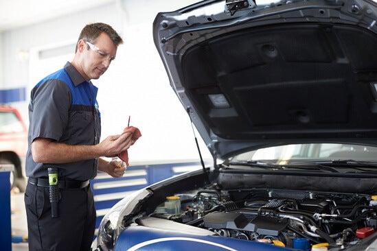 A mechanic working under the hood of a Subaru