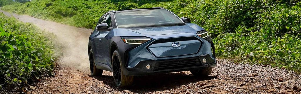 2026 Subaru Solterra driving on a gravel road with lush greenery surrounding it.