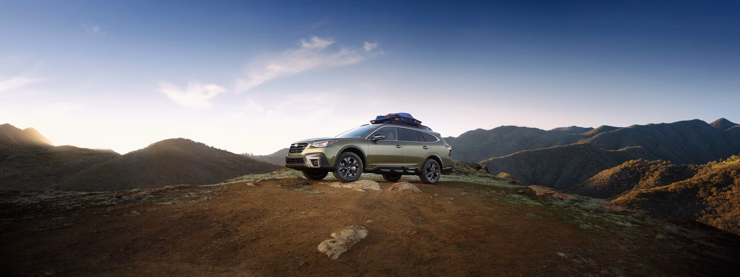 Subaru parked at the top of a remote hill at sunrise with gear on the roof