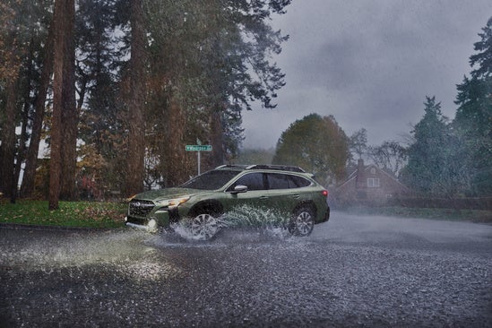 green Subaru driving through a deep puddle on a rainy day
