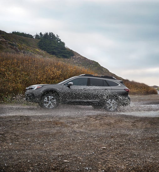 side view of a Subaru driving through a deep puddle on a rural road