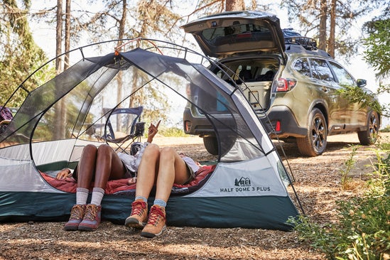 couple laying in their tent next to their Subaru