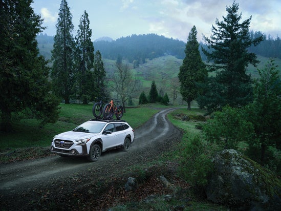 white Subaru with bikes mounted on the roof traveling through a rural road on a rainy day
