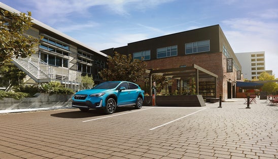 teal Subaru parked in front of a brick building on a sunny day