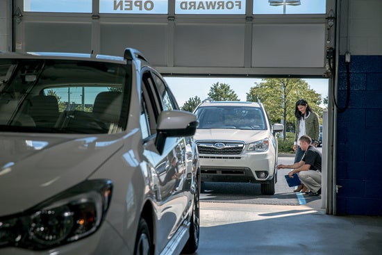 technician kneeling and looking at the tires of a customer's Subaru
