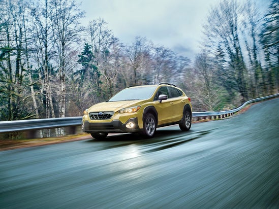 Subaru Crosstrek driving on a rainy day with headlights on a rural road
